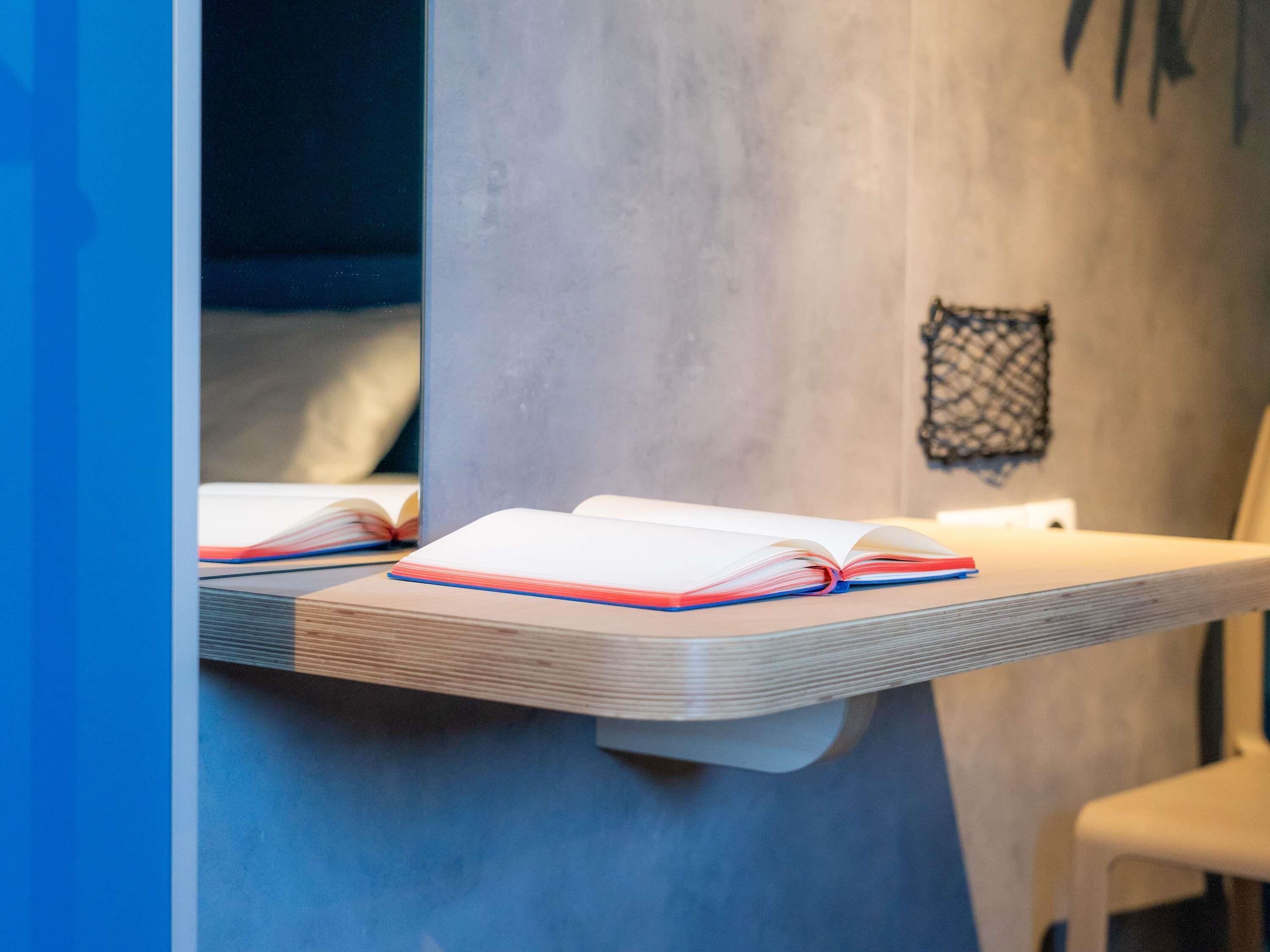 A room with a wooden shelf holding an open book, a chair, and a wall-mounted decorative item.