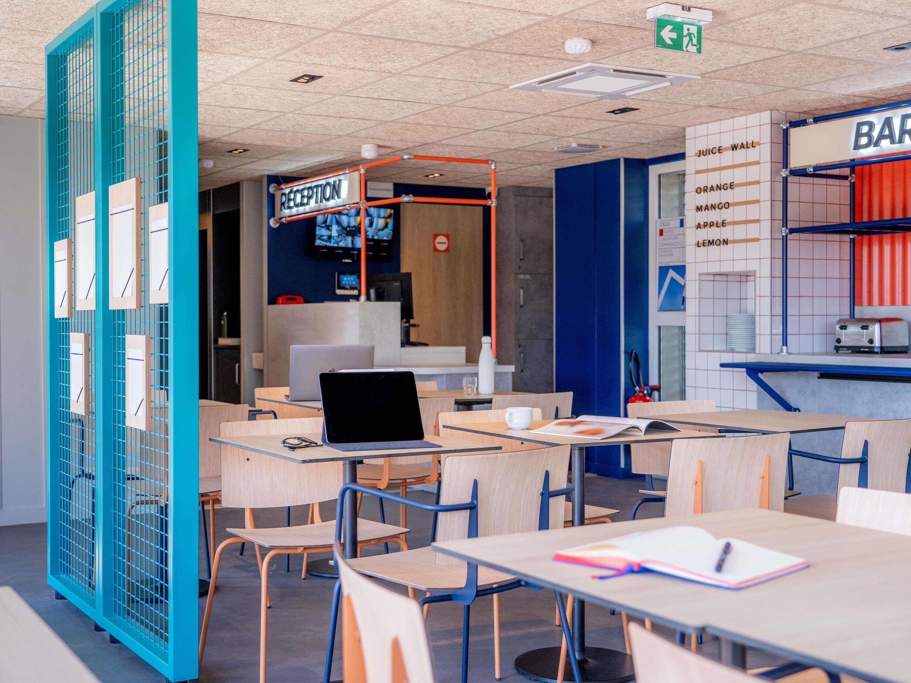 Un café moderne doté d’un comptoir d’accueil, de tables, de chaises et d’un mur dédié aux jus de fruits.