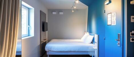 A modern hotel room with two single beds, a desk, and a window with curtains.