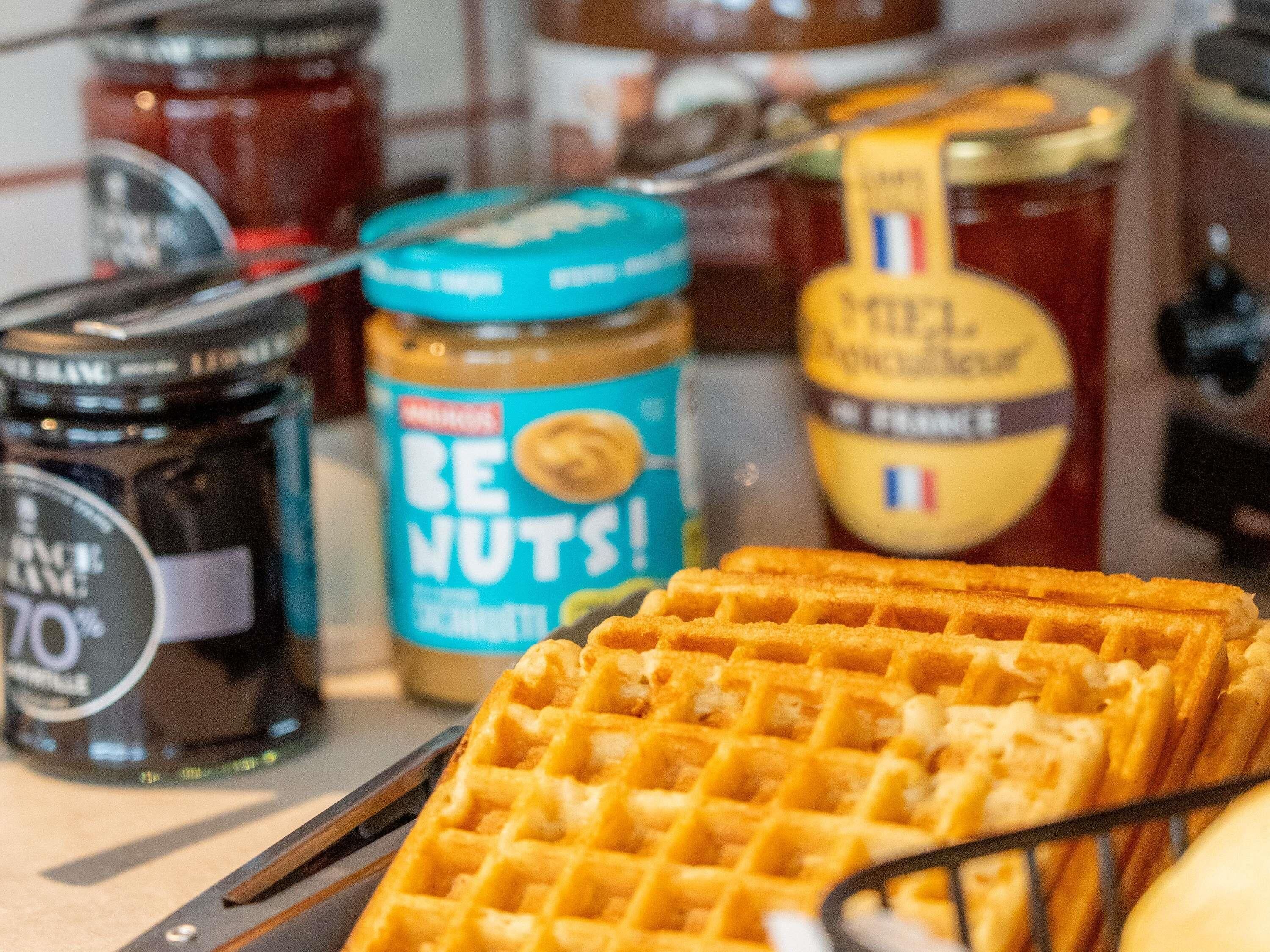 Une gaufre à motifs en losanges, entourée de pots de beurre de cacahuète et d’autres pâtes à tartiner.