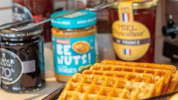 Une gaufre à motifs en losanges, entourée de pots de beurre de cacahuète et d’autres pâtes à tartiner.