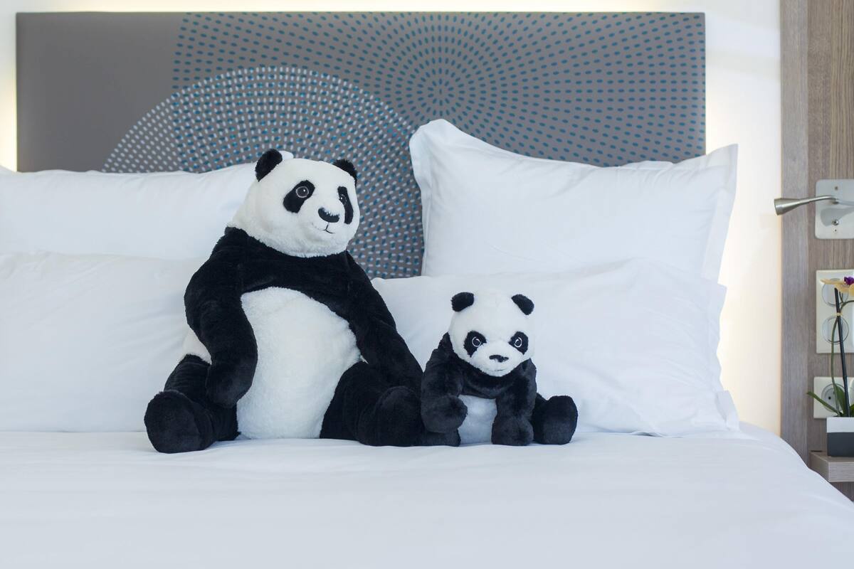 Un lit avec deux peluches panda, des oreillers blancs et une tête de lit moderne.
