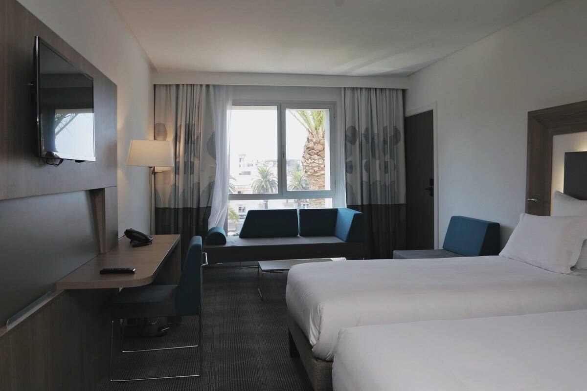 A hotel room with a bed, a desk, a chair, a TV, and a window with curtains.