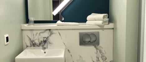 A bathroom with a white sink, a toilet, and a mirror with a light above it.