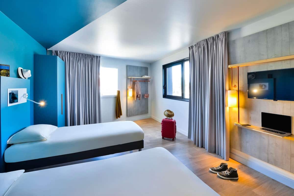 Ein modernes Hotelzimmer mit einem großen Bett, einem Schreibtisch, einem Fernseher und einem Koffer.