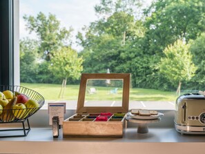 A breakfast setup with a fruit bowl, a wooden box of tea choices, and a vintage toaster. - ibis budget Mâcon Crêches (Chaintre)