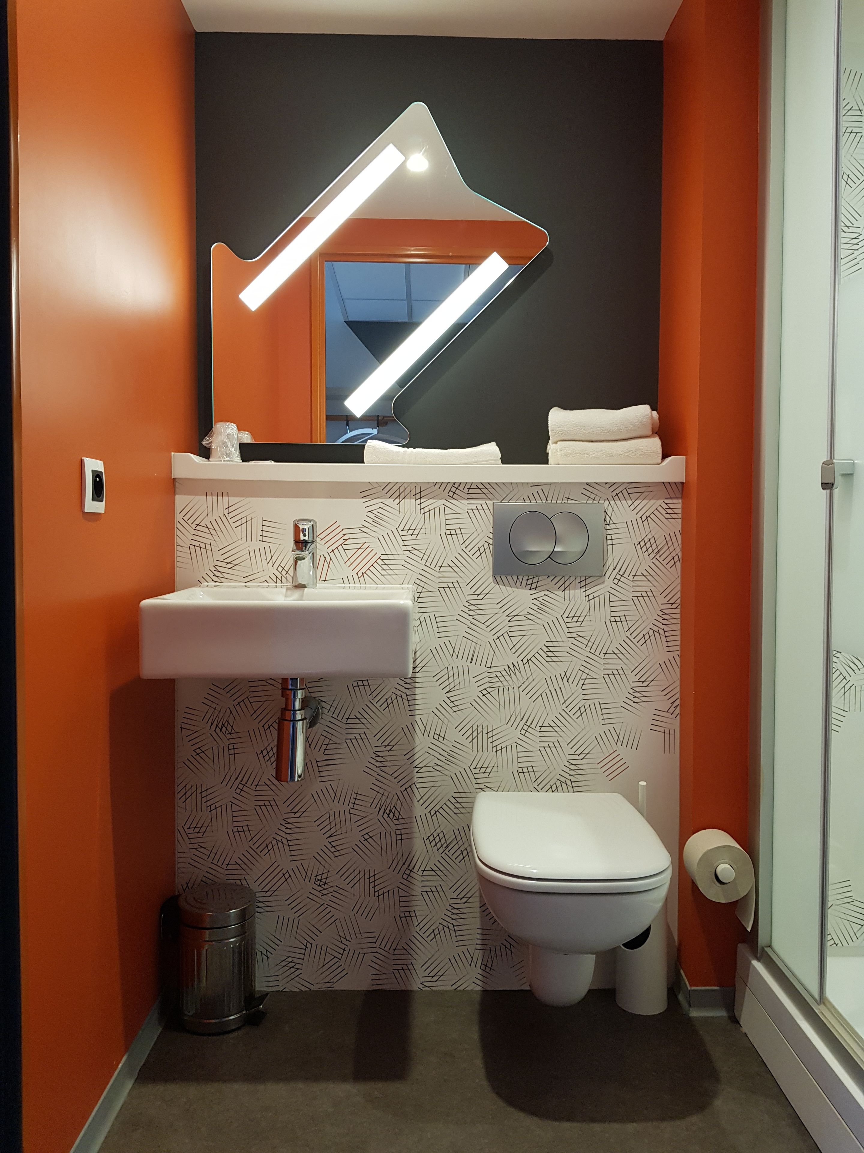 A bathroom with a white sink, a toilet, and a mirror with a modern light fixture.