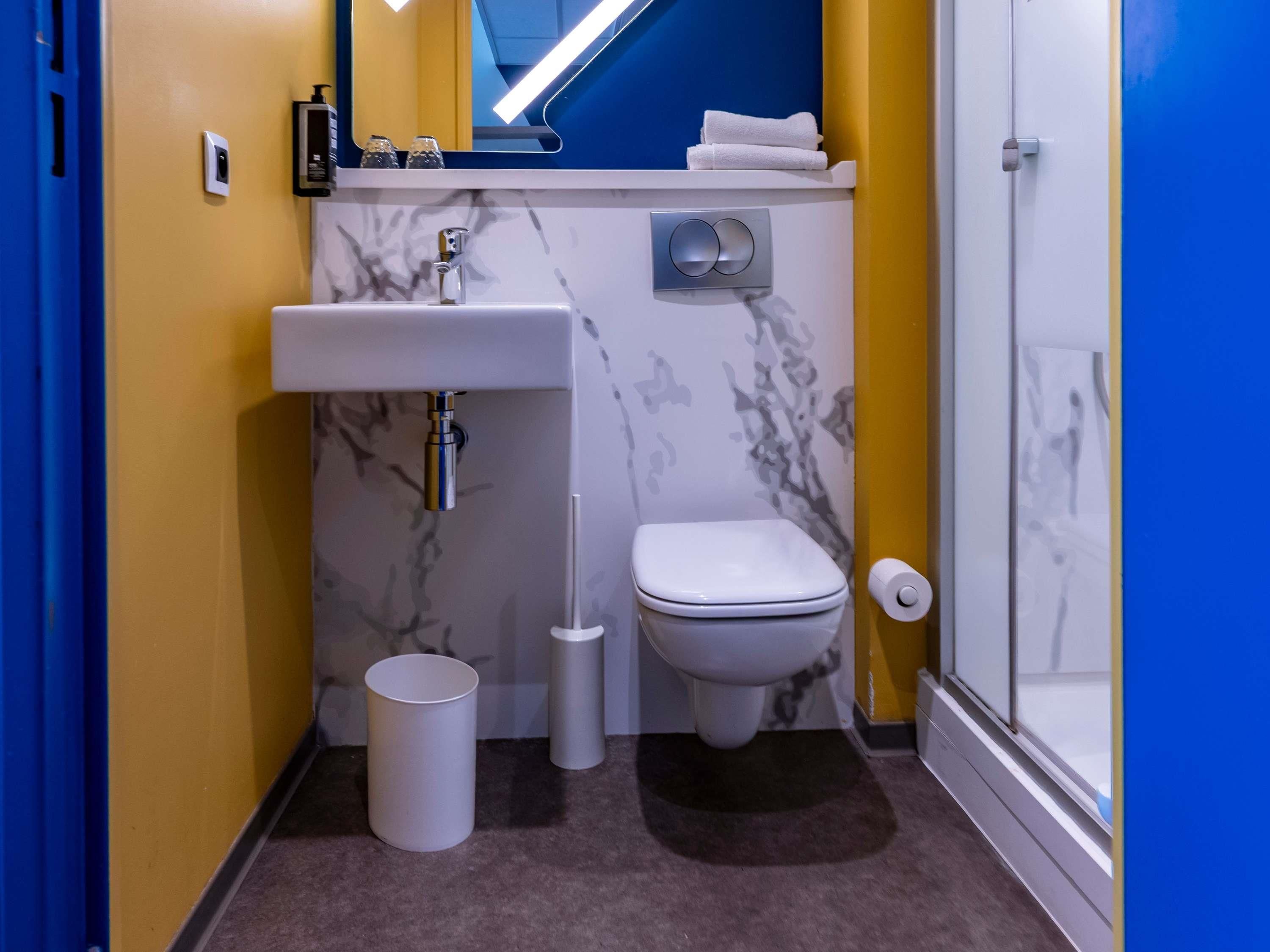 Une petite salle de bain avec un lavabo blanc, des toilettes et une petite poubelle.