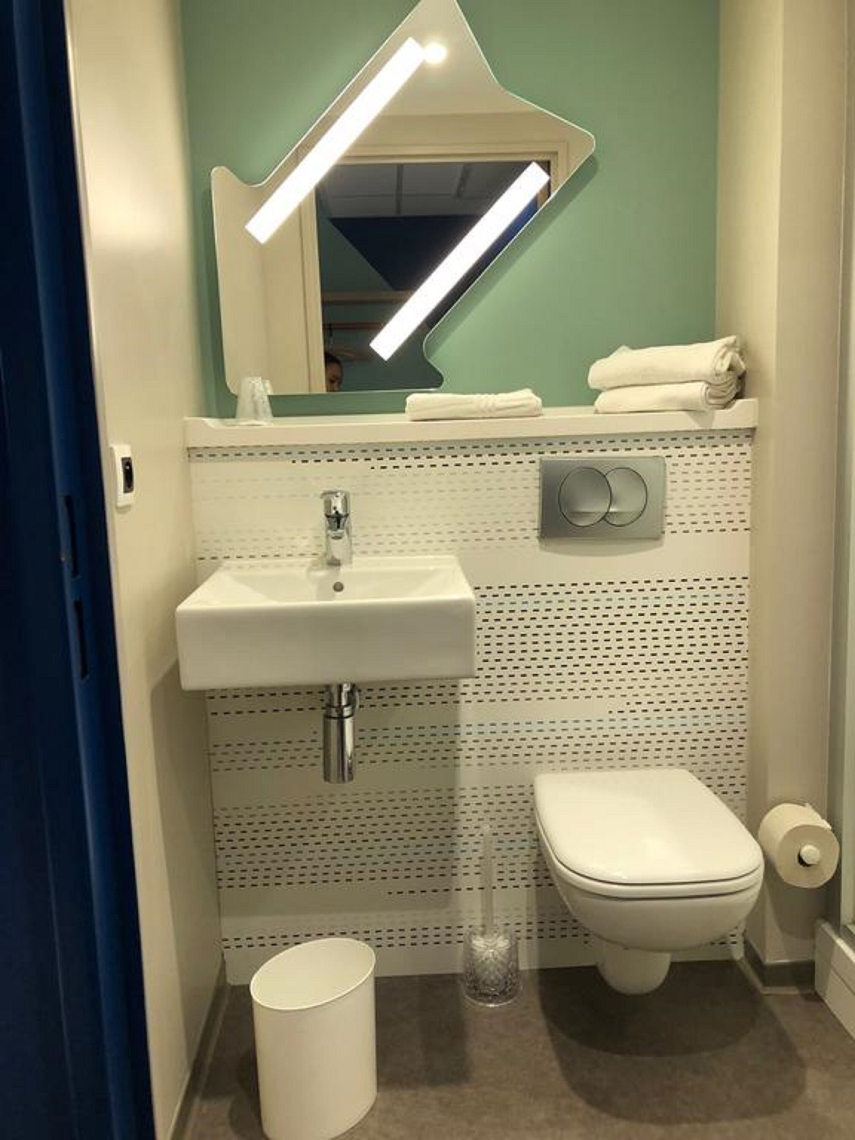 Une salle de bain avec un lavabo blanc, des toilettes, un miroir et un porte-serviettes.