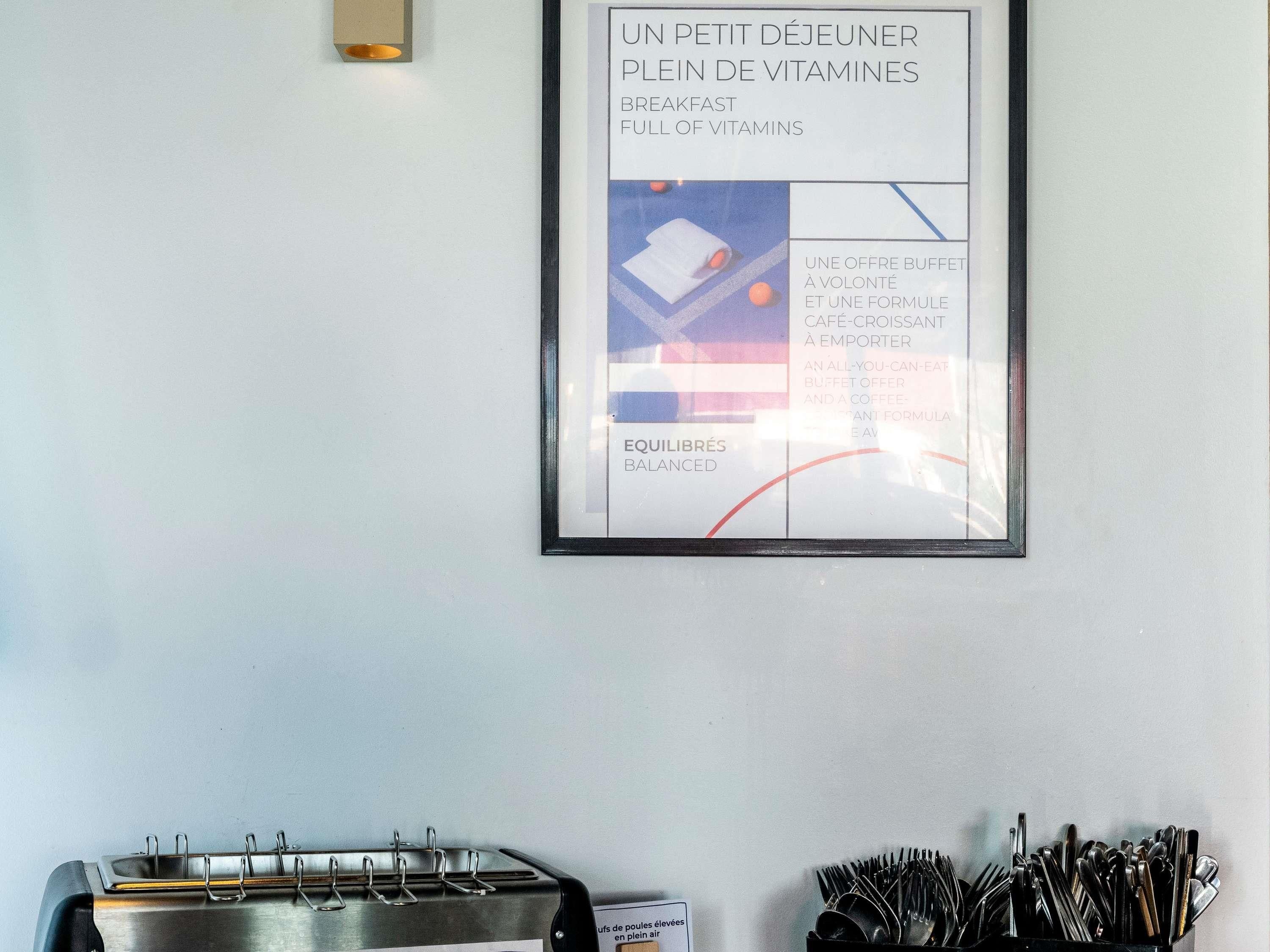 Un menu encadré présentant les options pour le petit-déjeuner et une formule café, un plateau en métal avec des couverts et un luminaire fixé au mur.