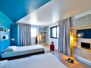 A modern hotel room with a large bed, a TV, a desk, and a suitcase. - ibis budget Mâcon Crêches (Chaintre)