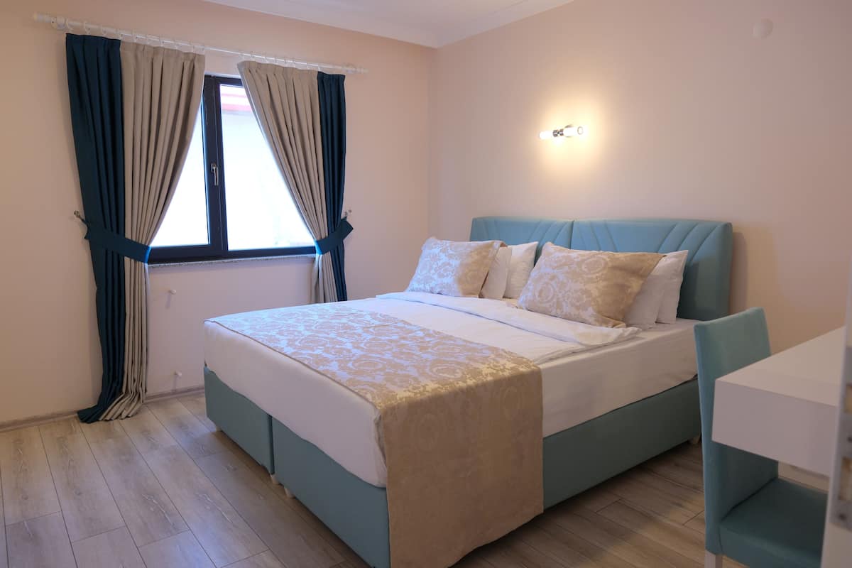 A bedroom with a bed, curtains, a bedside table, and a wall-mounted light.