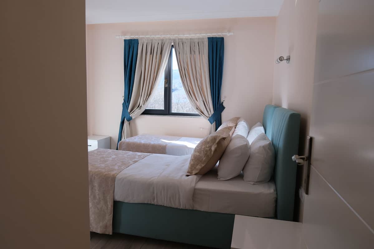 A bedroom with a bed, a nightstand, a window with curtains, and a wardrobe.