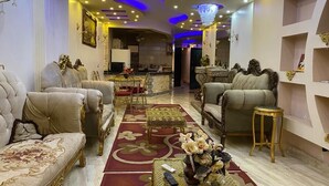Un salon luxueux, agrémenté de meubles richement décorés, d’un lustre et d’un tapis rouge.