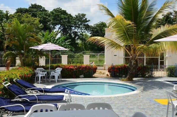A pool area with lounge chairs, a table, and umbrellas. - Condominio Atlantis (San Antero)