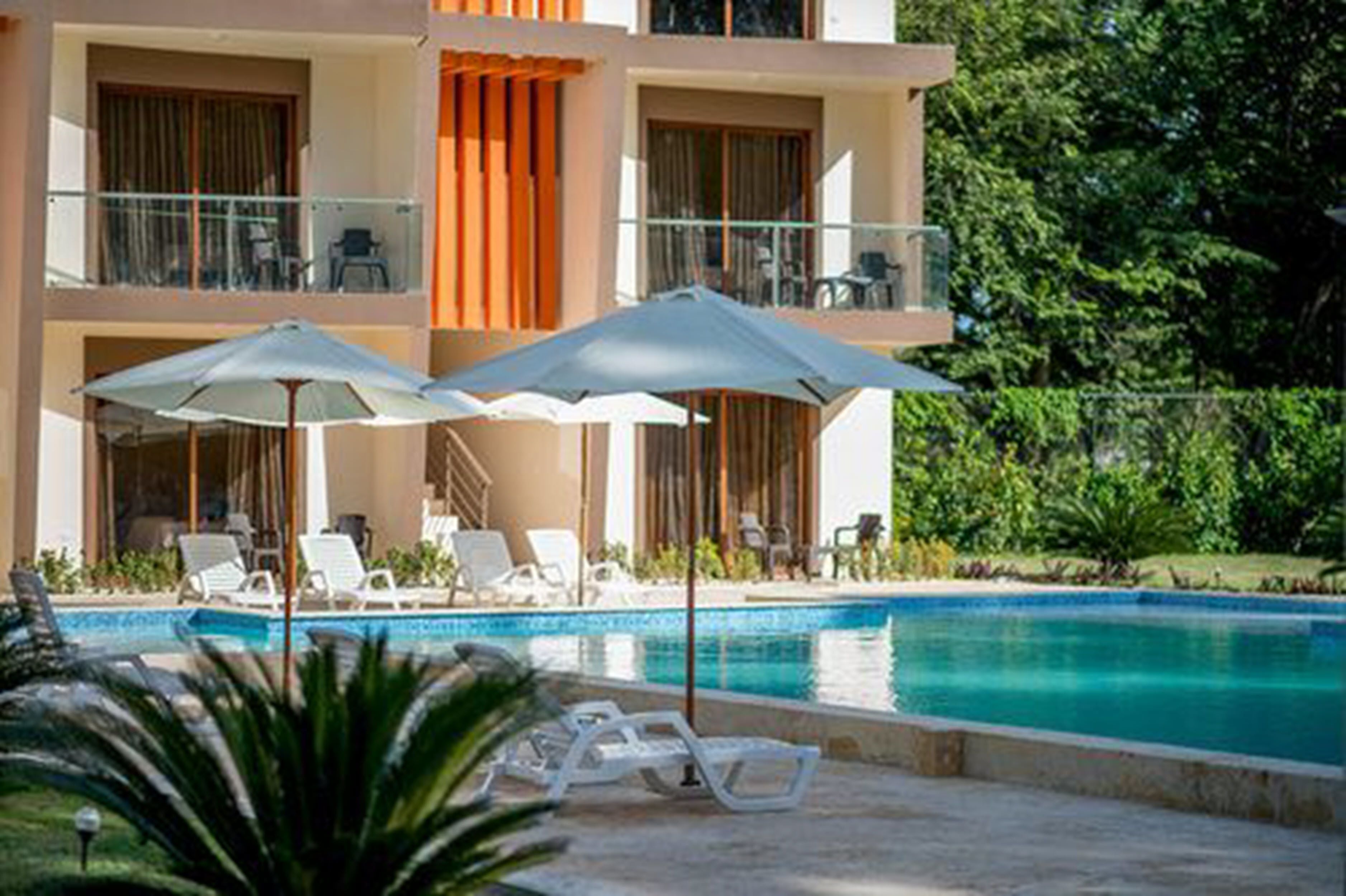 Un albergo con piscina, poltrone a sdraio e ombrelloni.