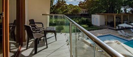 A balcony with a glass railing overlooking a swimming pool and outdoor seating area.