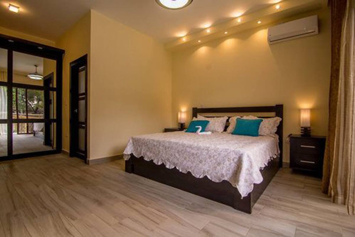 A bedroom with a large bed, a nightstand, an air conditioning unit, and a door leading to an outdoor area.