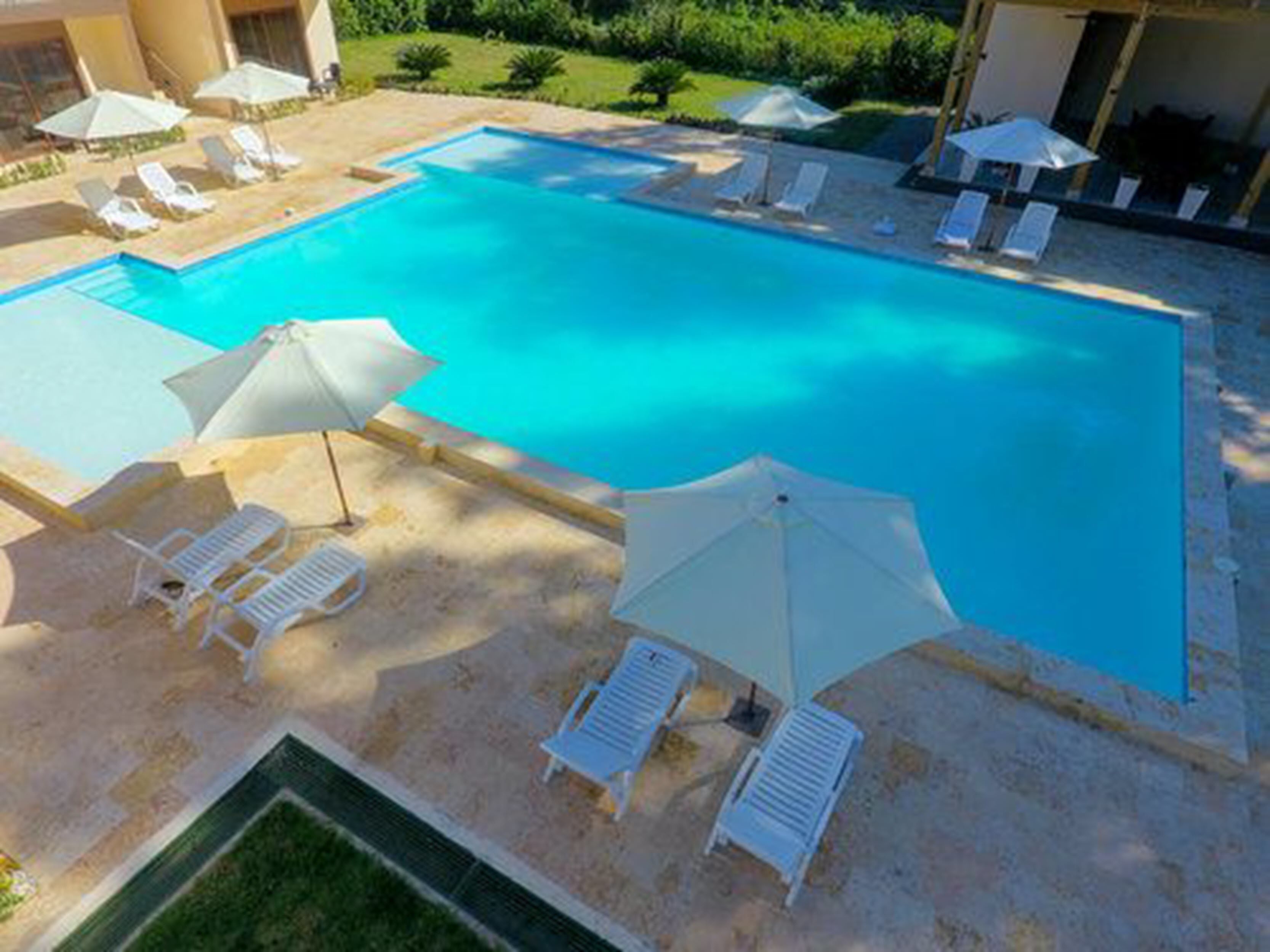 Ein Pool mit Liegestühlen und Sonnenschirmen, umgeben von einem angelegten Garten.