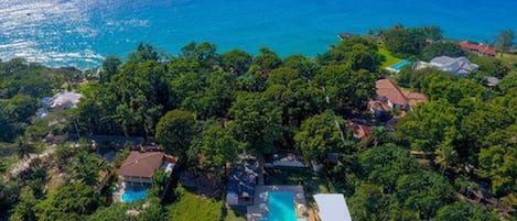 Vista aérea de una propiedad costera con piscina, abundante vegetación y vista al océano.