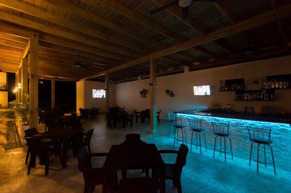 Zona de bar con piscina, techo de madera y taburetes.