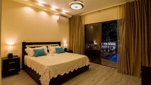 A bedroom with a large bed, a nightstand, a lamp, and a view of a pool through a glass door. - Caribbean Diamond Boutique Hotel (Sosúa)