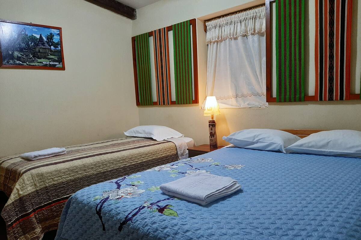 A hotel room with two beds, a nightstand, a lamp, and a framed picture on the wall.