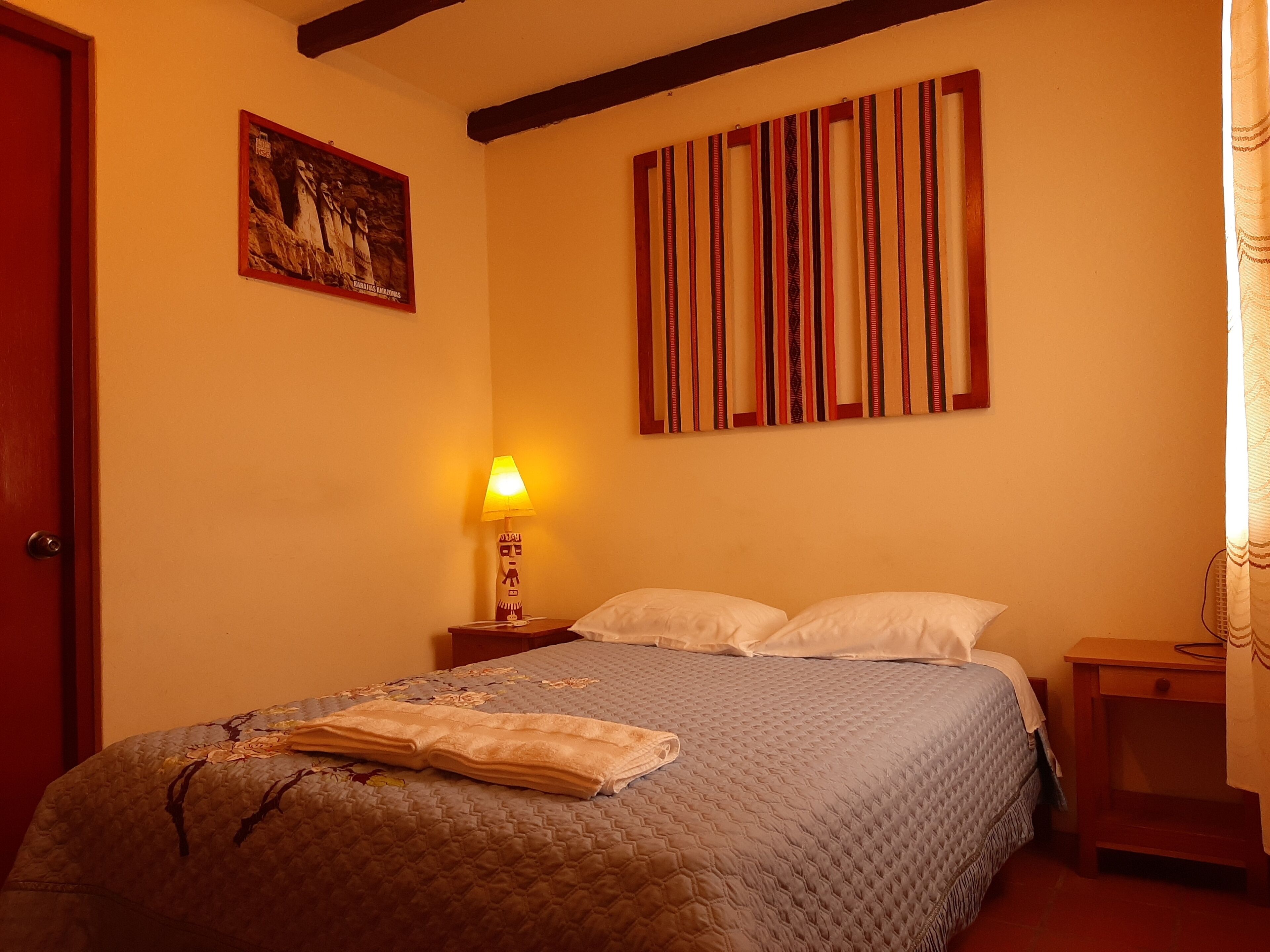 A hotel room with a bed, a nightstand, a lamp, a painting, and a striped curtain.