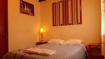 A hotel room with a bed, a nightstand, a lamp, a painting, and a striped curtain.