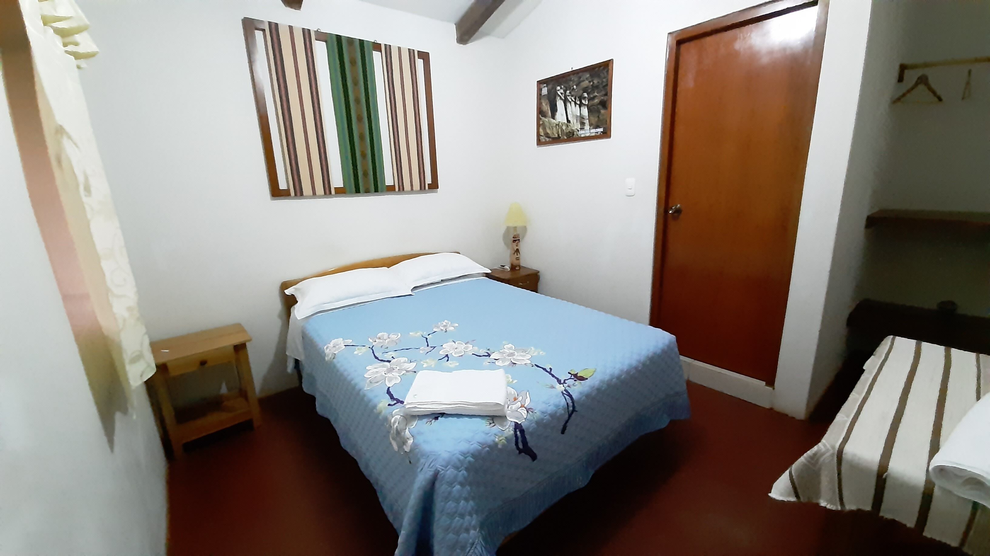 Une chambre à coucher comprenant un lit, une table de chevet, une lampe fixée au mur, une porte et une petite table.