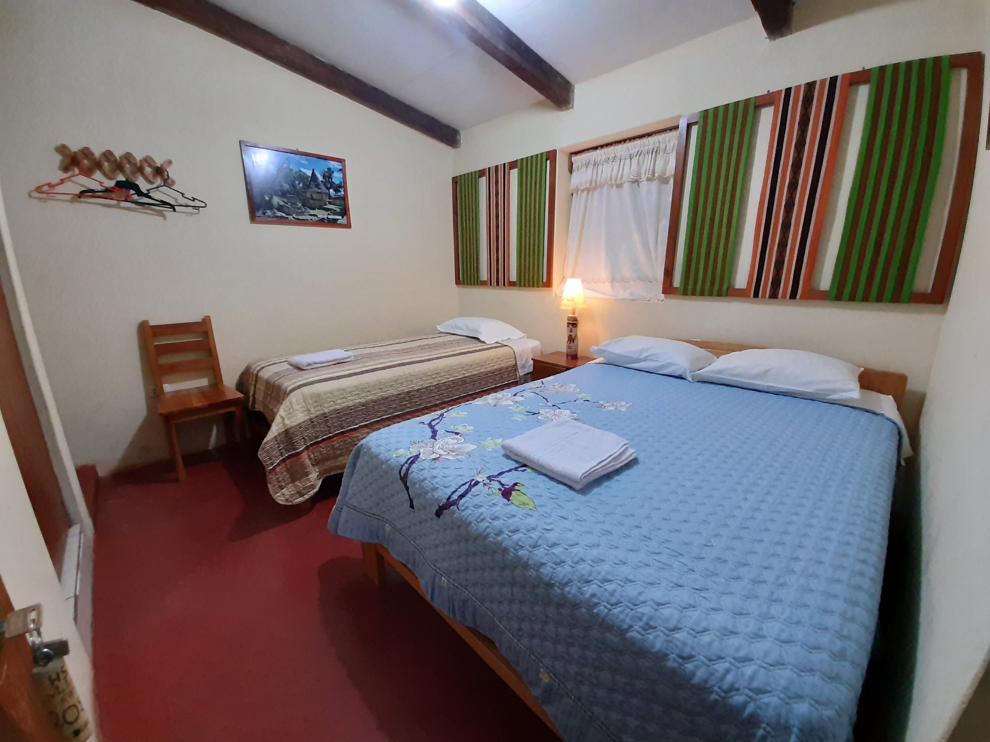 A bedroom with two beds, a chair, a bedside table with a lamp, and a picture on the wall.