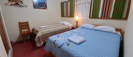 A bedroom with two beds, a chair, a bedside table with a lamp, and a picture on the wall.