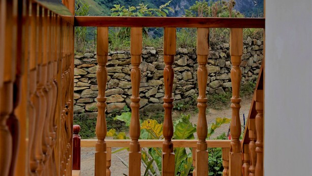 Un balcon en bois, avec un mur en pierre et une vue sur un paysage montagneux agrémenté d’une cascade.