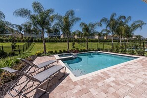 A swimming pool with a tiled deck, surrounded by palm trees and a well-maintained lawn.