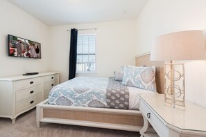 A bedroom with a bed, dresser, and a TV on the wall.