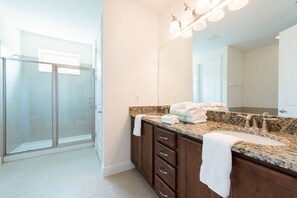 A modern bathroom with a glass shower enclosure, a granite countertop, and a large mirror.