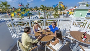 A group of people seated at a round table with a view of a water park and beach in the background. - New House, Near Disney, Private Pool (Kissimmee)