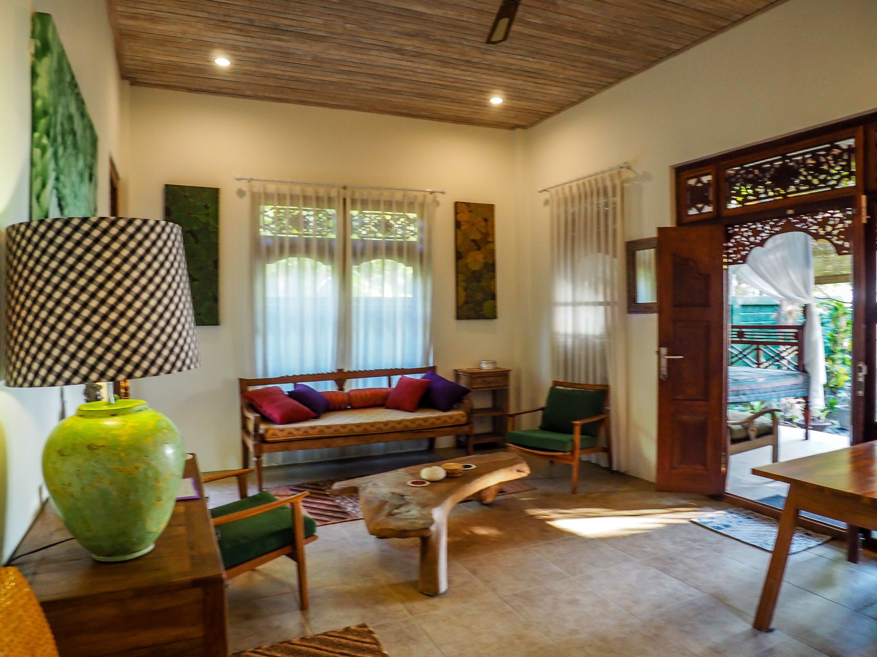 A cozy living room with a wooden ceiling, a green sofa with colorful cushions, a wooden coffee table, and a large green vase.