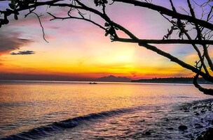 Un atardecer sobre un mar tranquilo con la silueta de montañas a lo lejos.