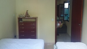 A bedroom with two beds, a wooden dresser, and a door leading to another room. - Casa em Cabo Frio (Cabo Frio)