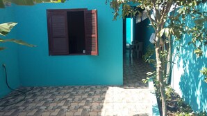A narrow outdoor corridor with a tiled floor, a window with brown shutters, and a blue wall. - Casa em Cabo Frio (Cabo Frio)