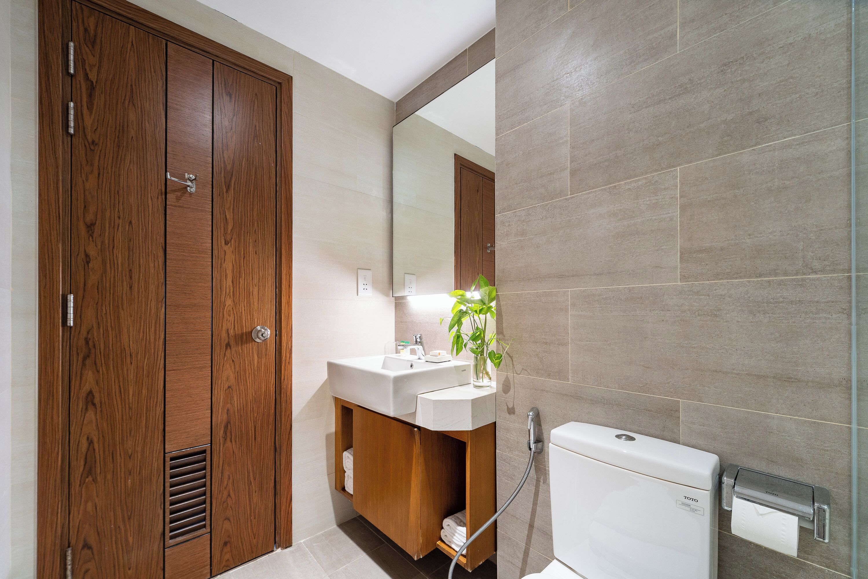 A modern bathroom with a wooden vanity, a white toilet, and a mirror.