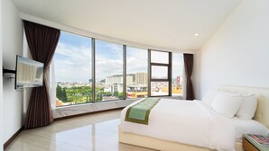A modern hotel room with a large bed, a flat-screen TV mounted on the wall, and a city view through large windows. - DIC Star Landmark Vung Tau (Ho Chi Minh City)