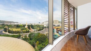 A room with a large window overlooking a cityscape, a curved wall, and a brown chair. - DIC Star Landmark Vung Tau (Ho Chi Minh City)