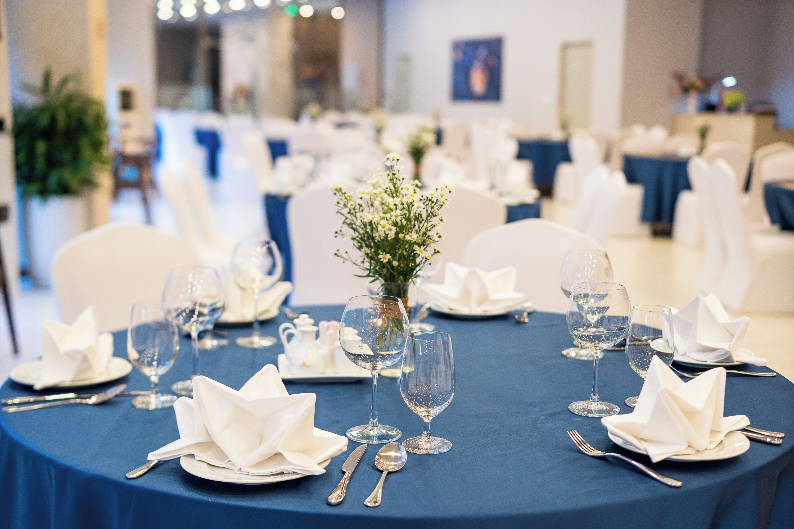 A dining table set with white napkins, silverware, and clear glassware, surrounded by white chairs.