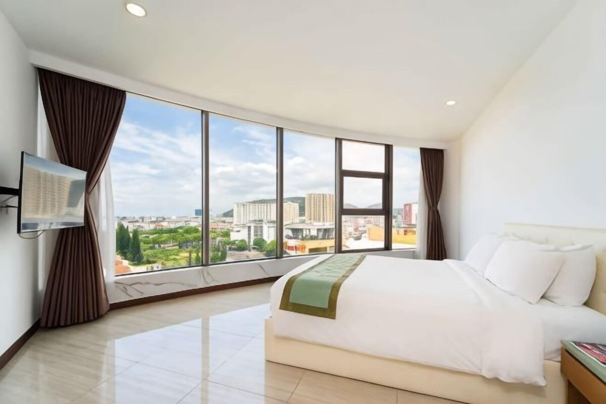 A hotel room with a large bed, a flat-screen TV, and a city view.