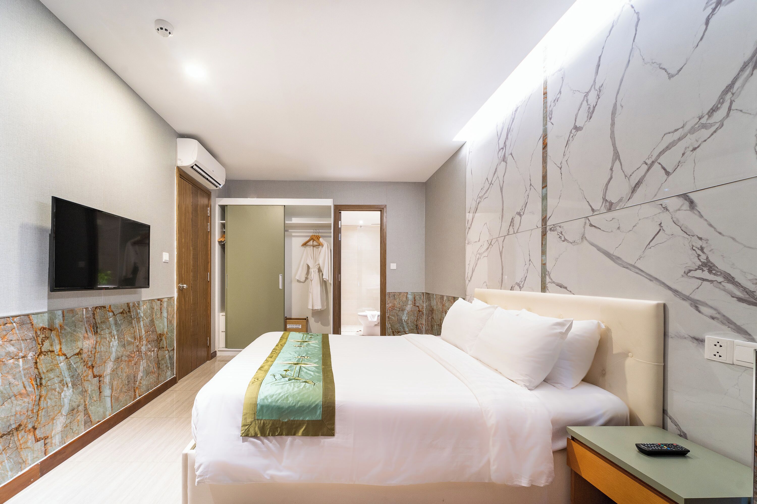 Habitación de hotel con una cama grande, un televisor montado en la pared y un revestimiento de pared con diseño de mármol.