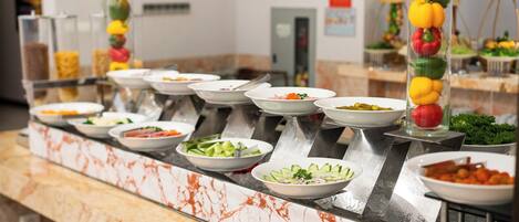 Un bufé con diversas opciones de comida, entre ellas ensaladas y verduras, dispuesto sobre una encimera de mármol.