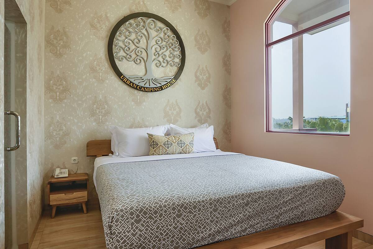 A neatly made bed with a patterned bedspread, a bedside table with a phone, and a wall-mounted tree decoration.