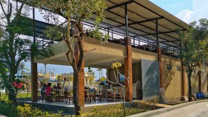 Un café al aire libre con zona de estar cubierta, rodeado de árboles y plantas.